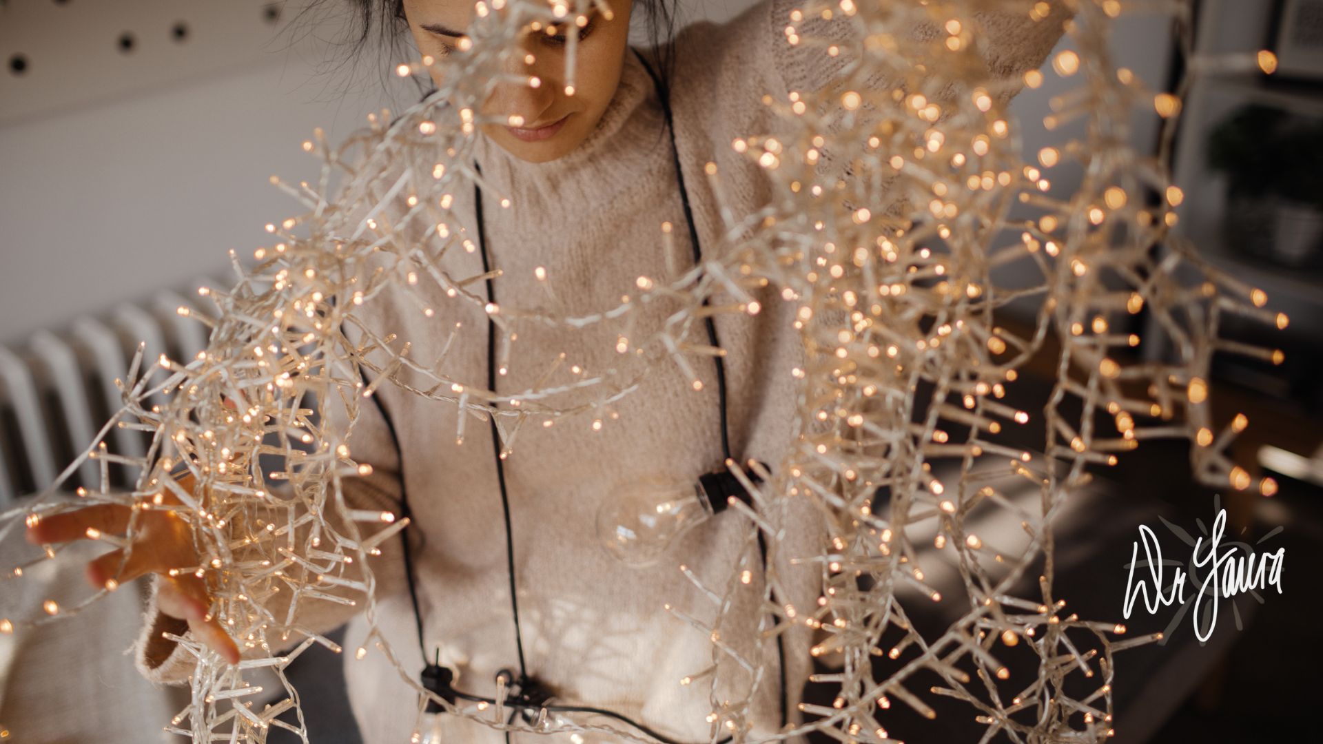 Woman wearing a white sweater holds up string lights