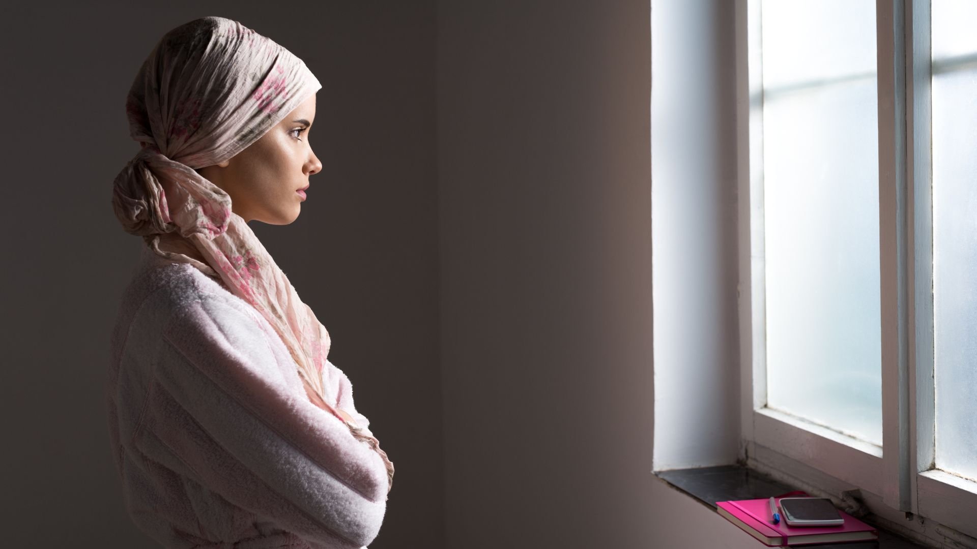 Woman with headscarf crosses her arms while looking out of window
