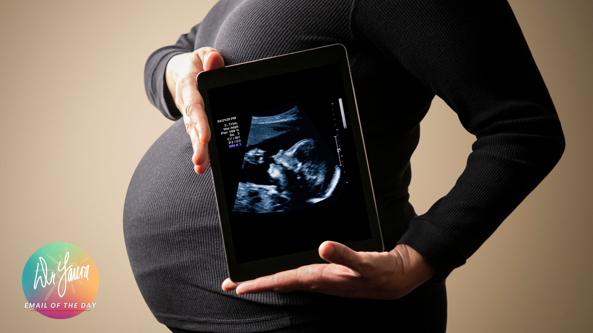 Pregnant woman in grey shirt holds tablet with uterus image in front of her belly