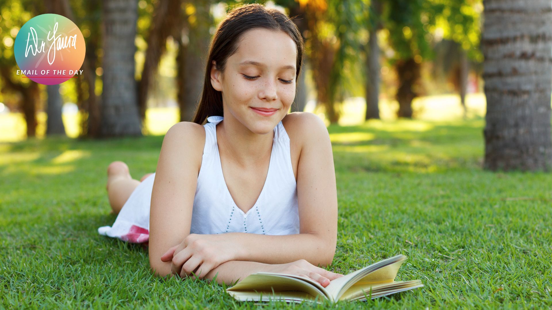 Teen girl in white dress lays on grass and reads open book in front of her