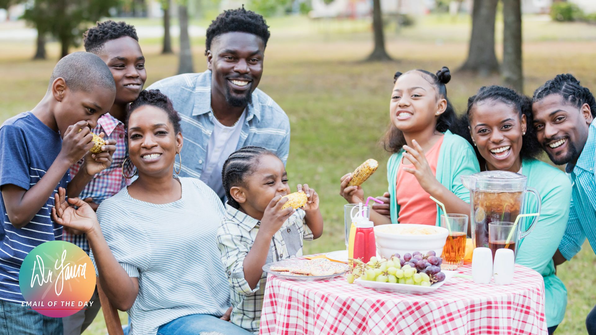 Family sits around table outside, eating food and smiling