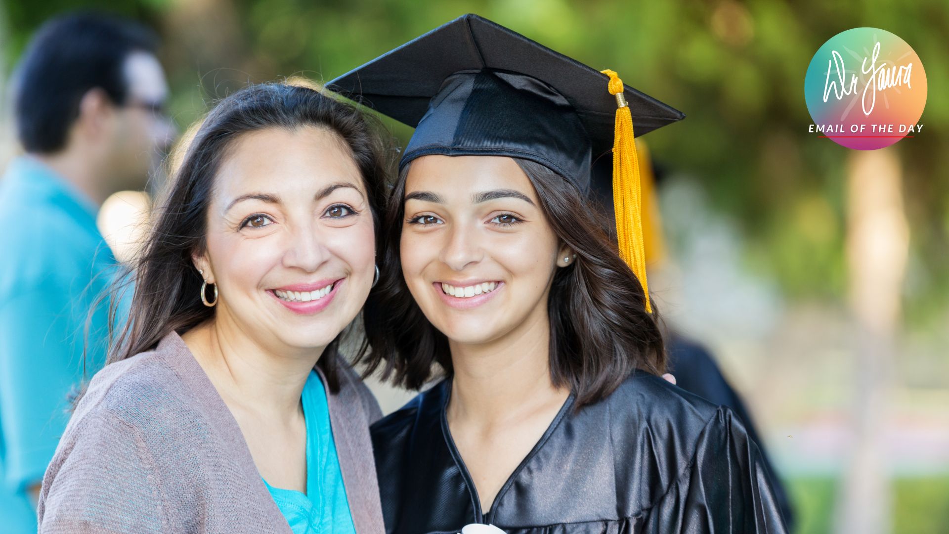 Young woman in graduation gown and cap smiles with woman in grey cardigan smiling next to her