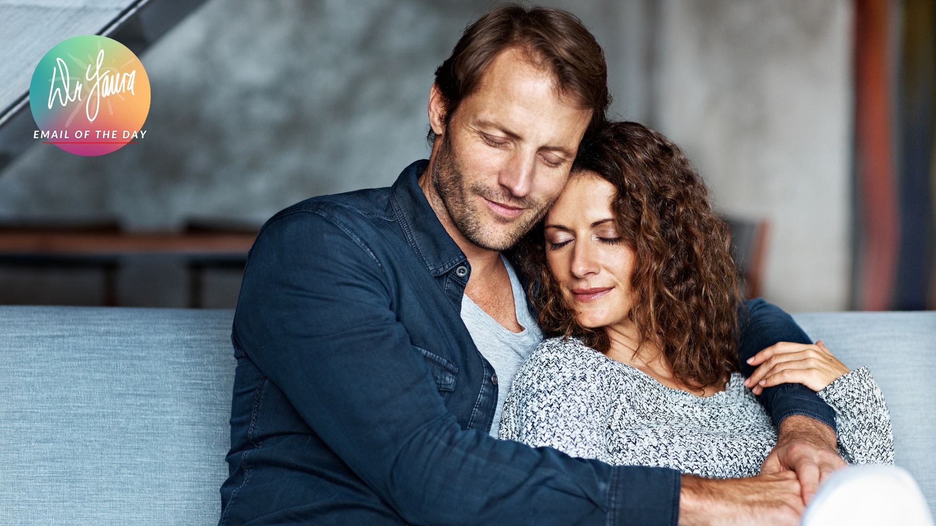 Man embraces woman around the shoulders, both with eyes closed and sitting on couch