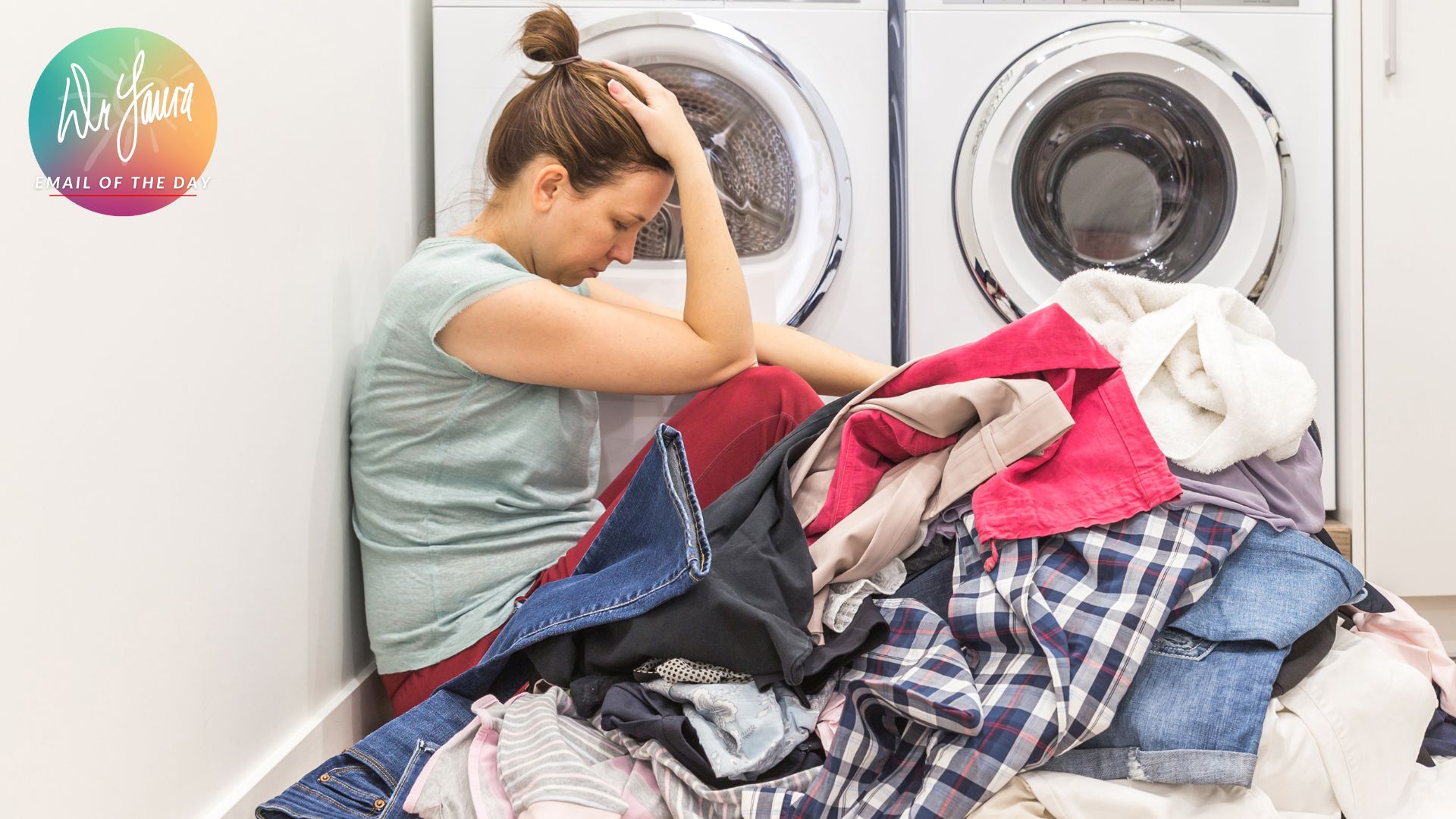 Woman sits on ground in laundry room while head in her hands in front of a pile of clothes
