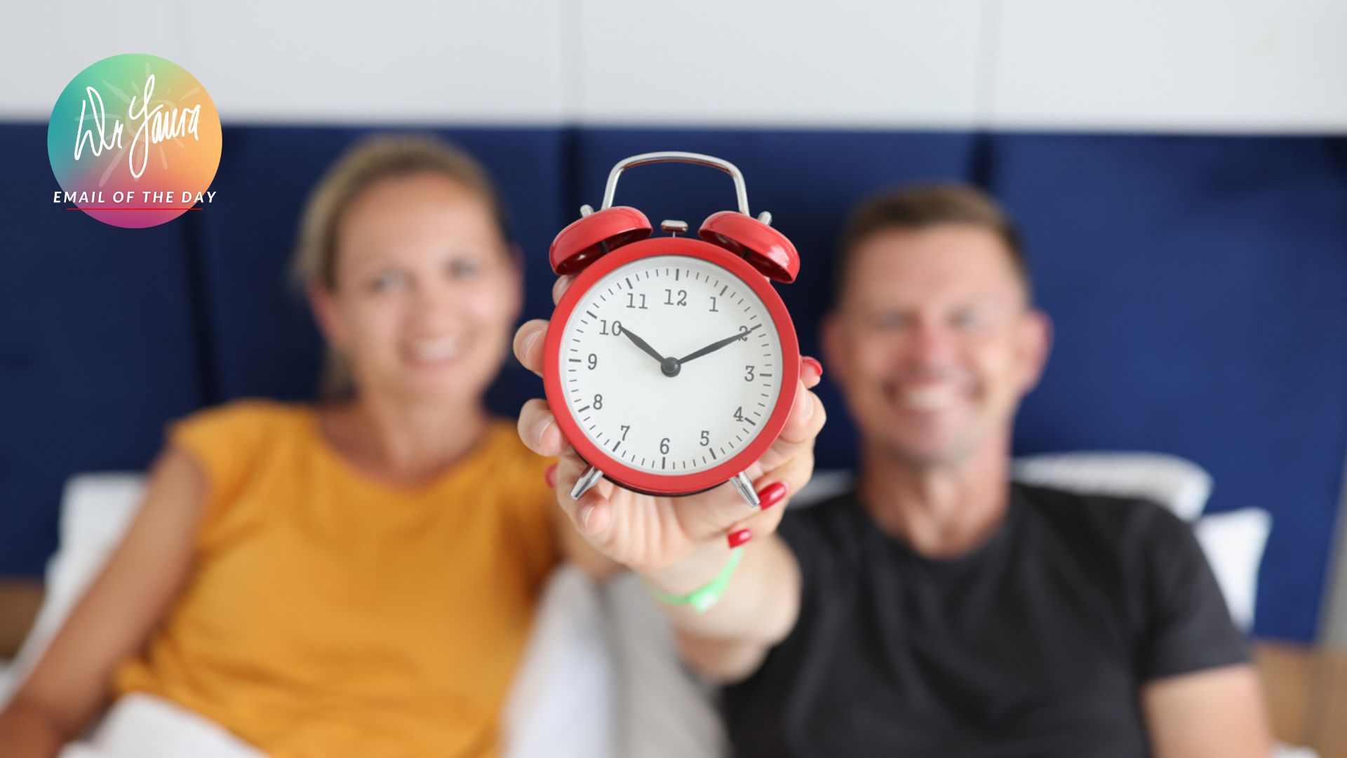 Woman and man both hold onto red alarm clock while sitting up in bed