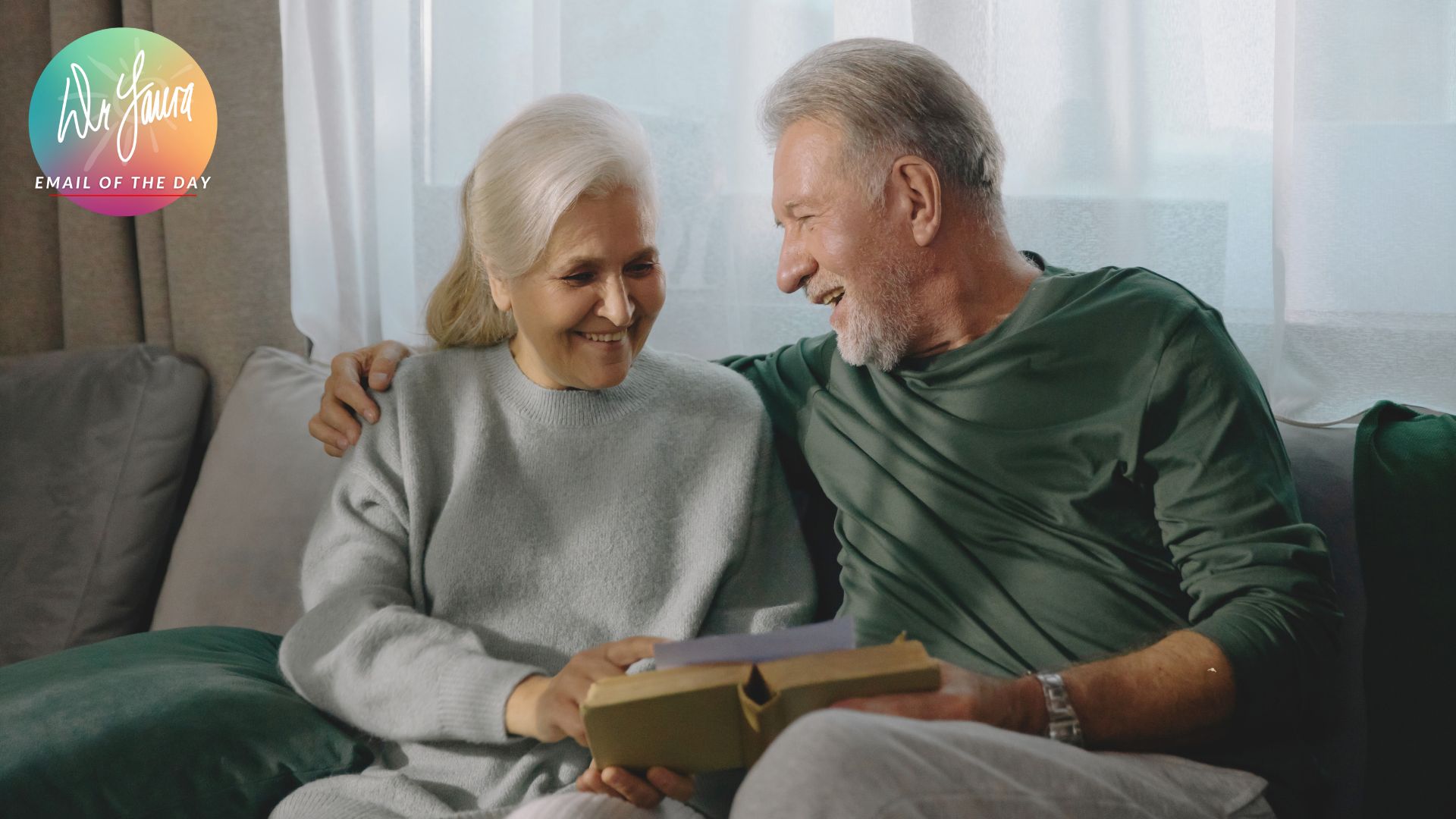 Older man and woman sit next to each other on the couch, both looking at a book together