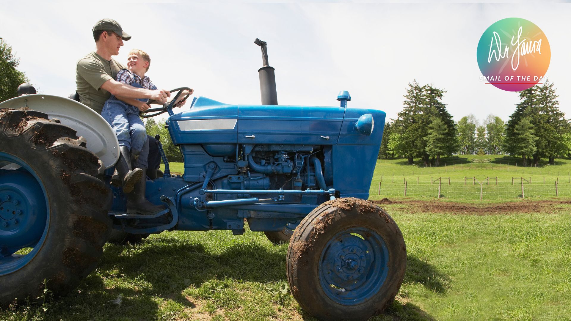 Man and boy sit on blue tractor while riding in the field