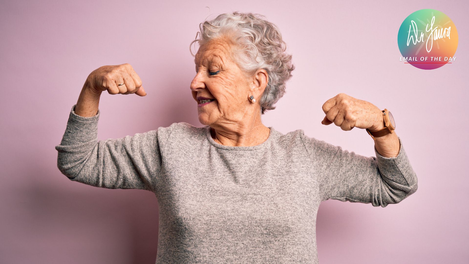 Older woman in grey shirt flexes her biceps while looking down at right arm
