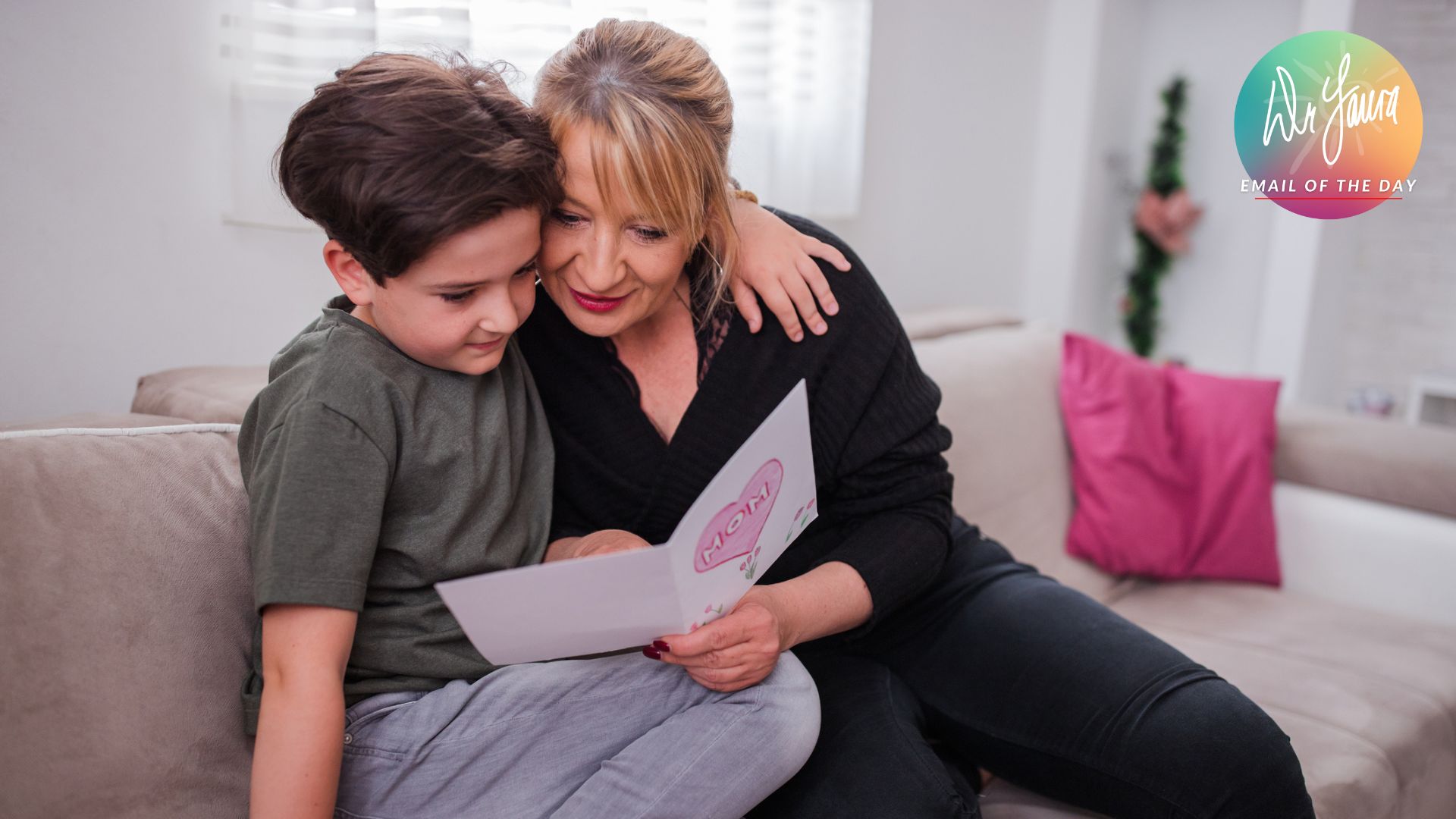 Young boy hugs mom while both of them sit on the couch and read card together