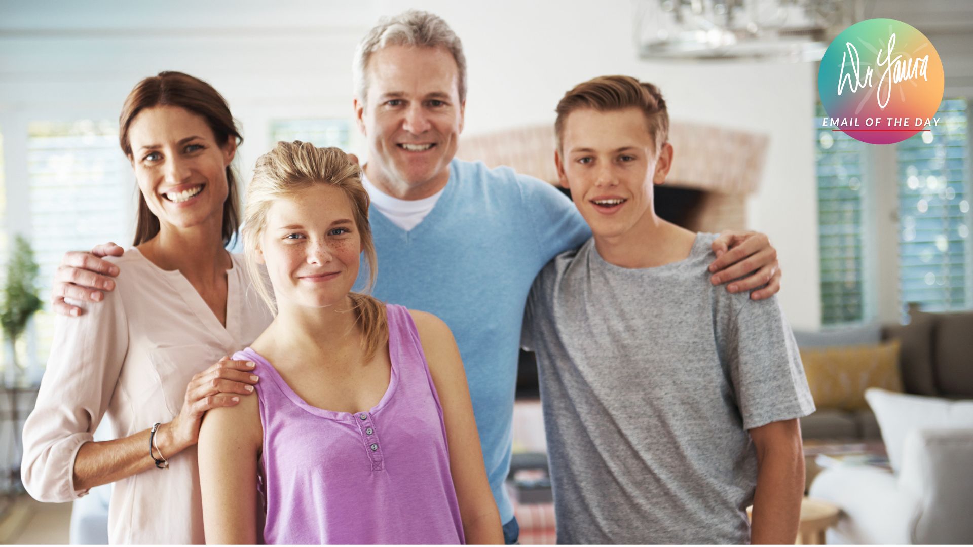 A family of four (mom, dad, young woman and young man) smile and stand with each other