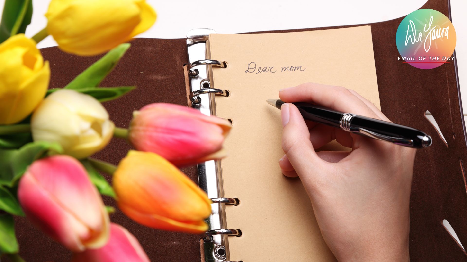 Hand holds pen while writing in notebook, "Dear mom," with tulips on the left side
