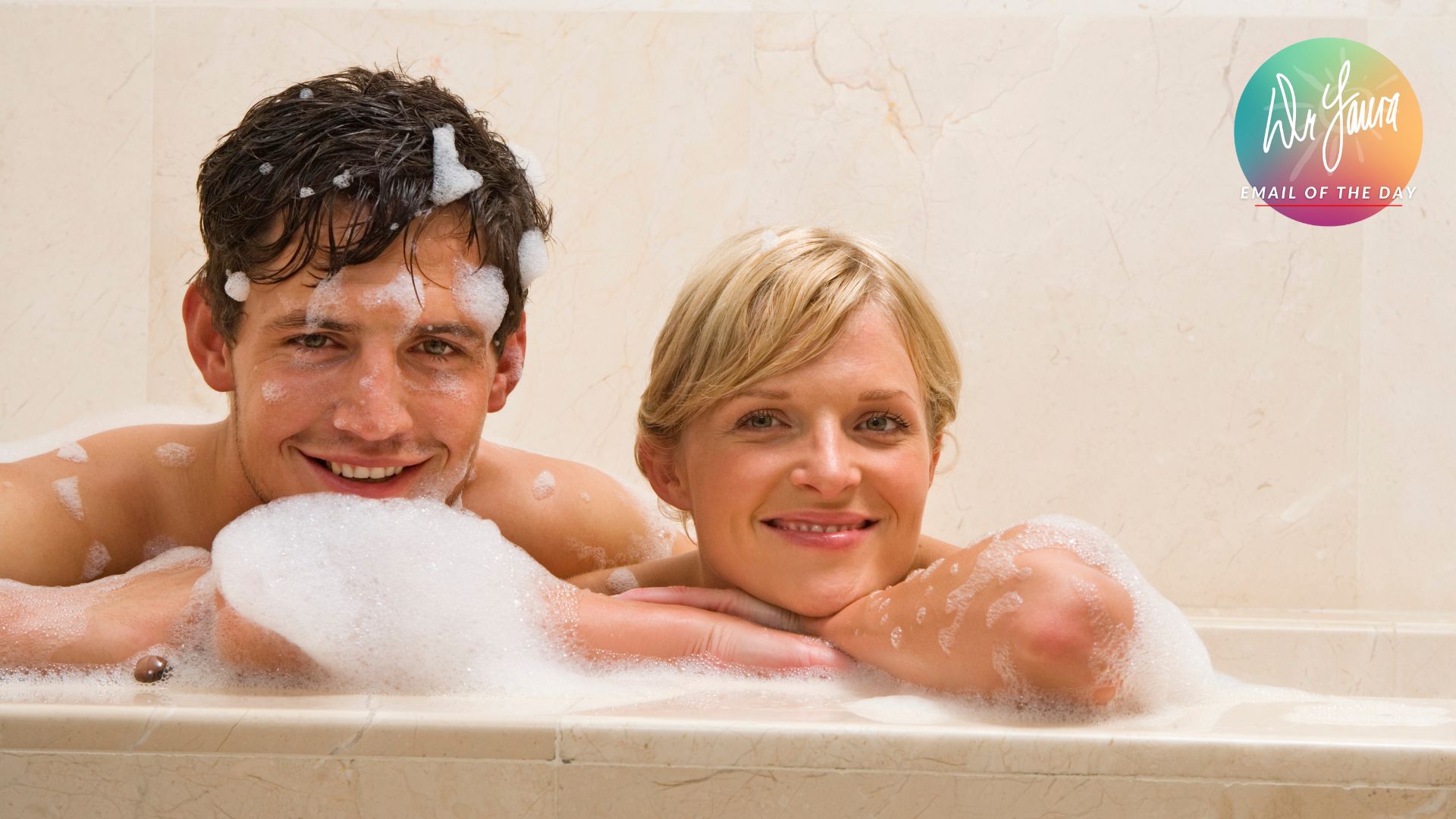 Woman rests head and arms on the edge of the tub while man sits next to her smiling