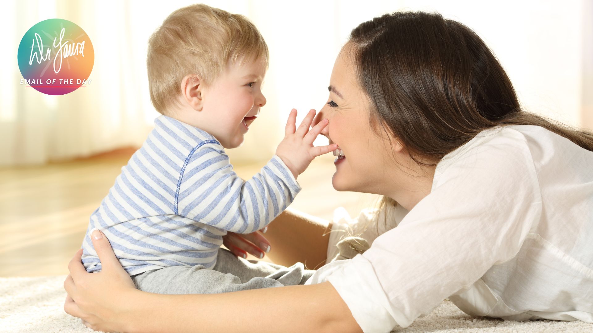 Smiling woman laying down embraces baby sitting down and touching the woman's nose