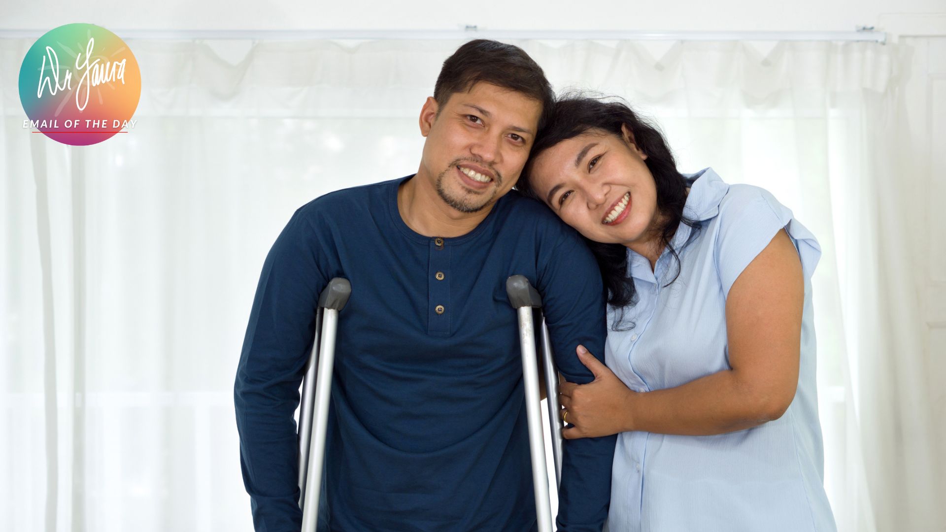 Smiling man stands on crutches while smiling woman holds onto one of his arms and leans head on his shoulder