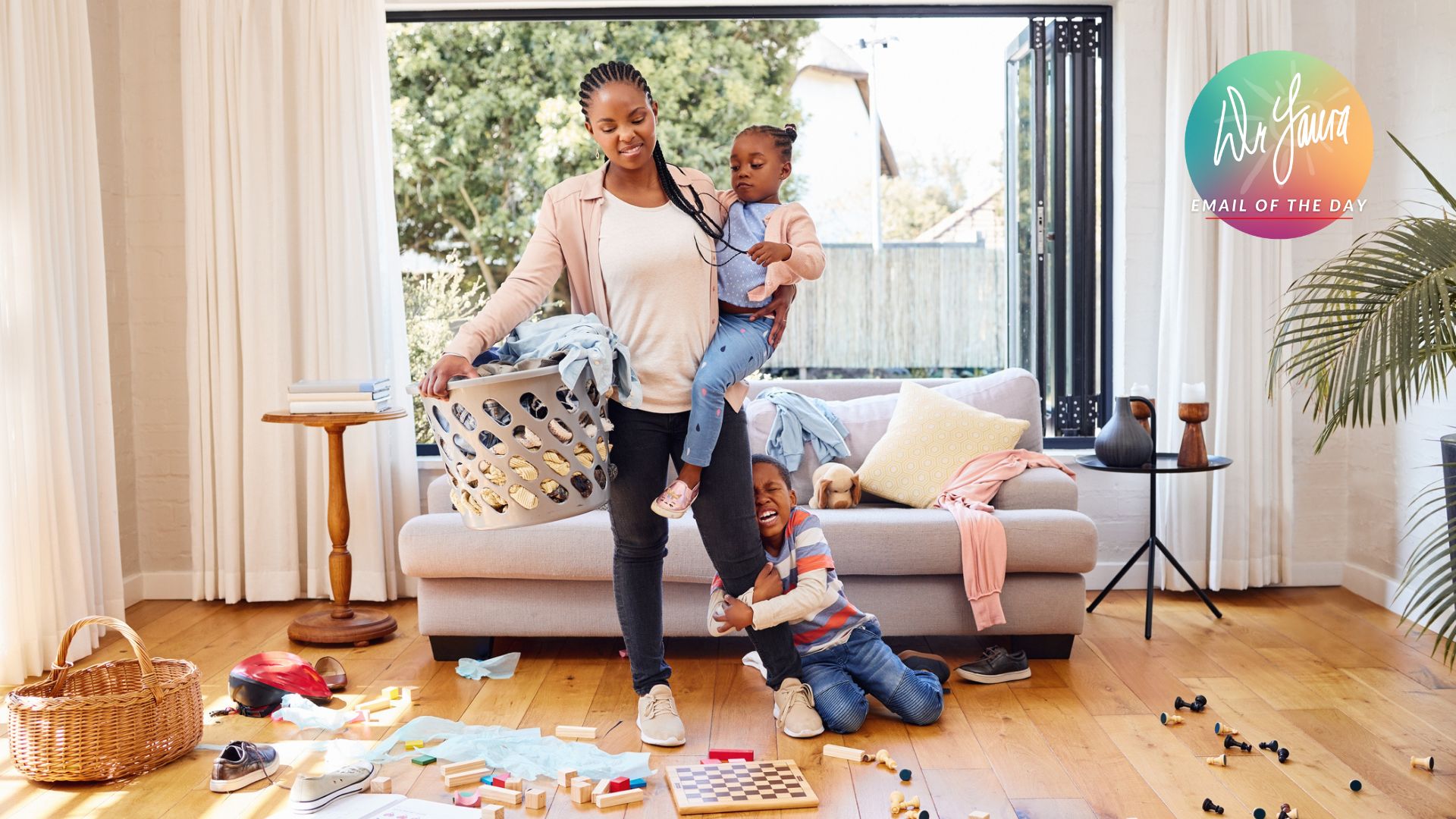 Woman carries toddler in messy living room while young girl hangs onto one of the woman's legs