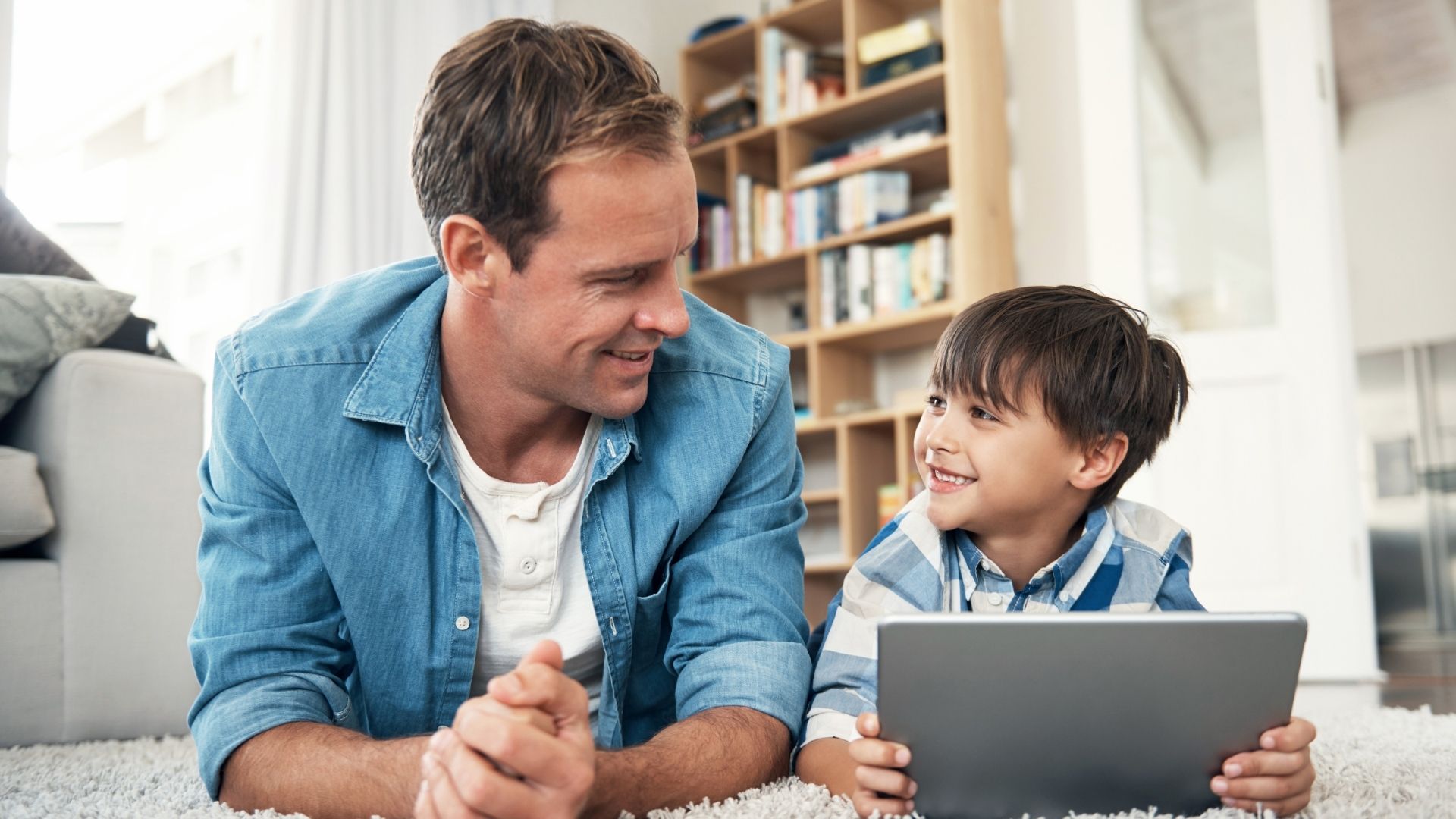 Young boy holds onto smart tablet while looking at older man who is sitting next to him